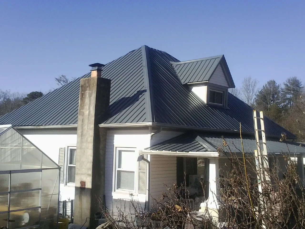 Dark blue standing seam metal roof on a white farmhouse with dormer — Slate & Tile Roof Repair by Roofing Brothers in Ludowici