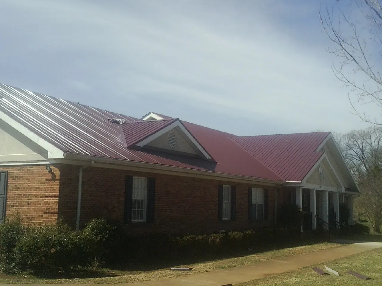 Red metal roof with gabled entries on a long brick building, from a Hail Damage Roof Repair job in Ludowici