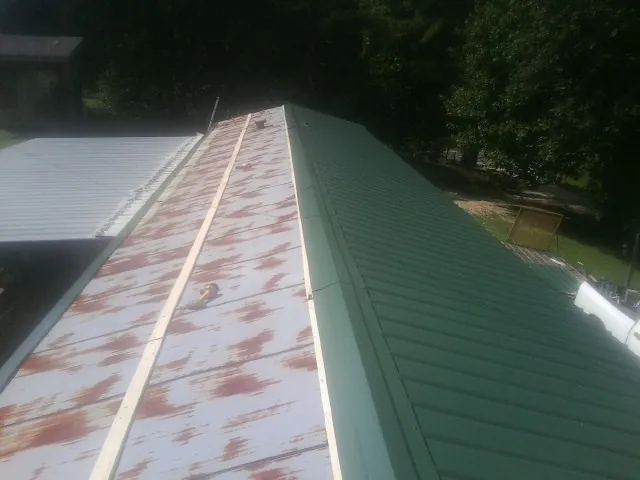 Old rusted panels beside newly installed green metal roofing — Wind Damage Roof Repair by Roofing Brothers in Ludowici
