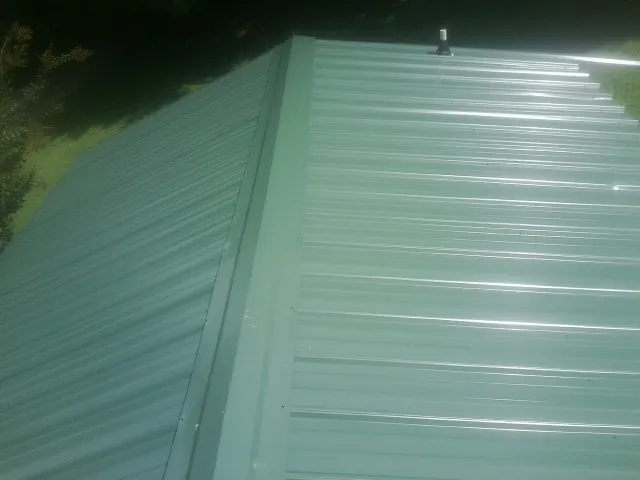 New green metal panels meeting at the ridge of a roof — Flat Roof Repair work by our crew in Ludowici