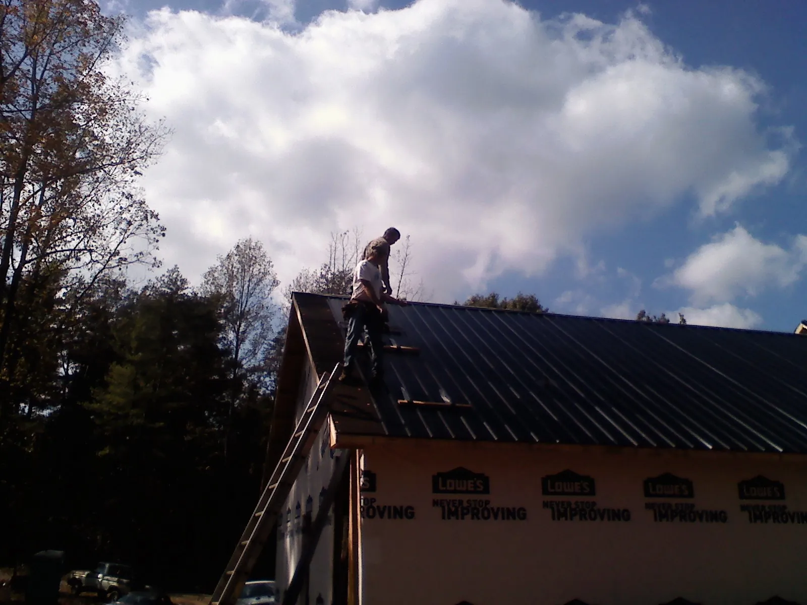 Roofer fastening dark metal panels high against a cloudy sky, from a Roof Inspection job in Ludowici