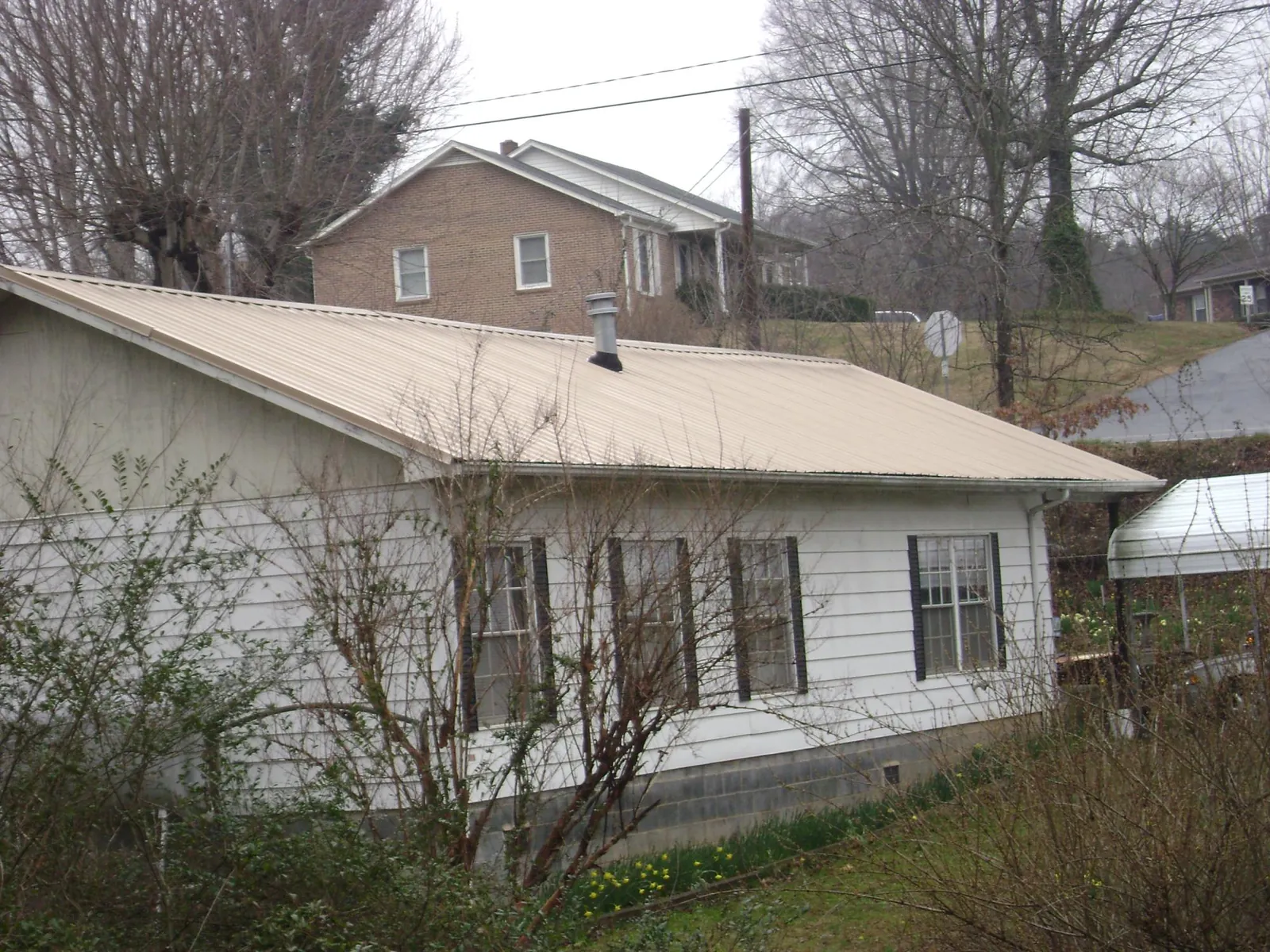 Tan metal roof on a white sided house set into a hillside — Commercial Roofing by Roofing Brothers in Ludowici